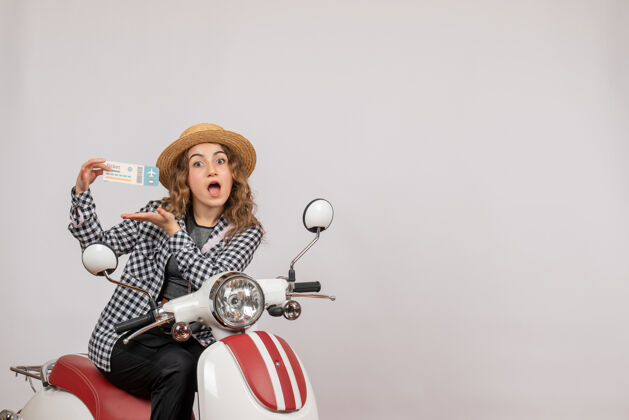 人骑着轻便摩托车的年轻女子拿着灰色的车票大吃一惊车辆惊喜少女肖像