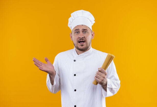 意大利面年轻帅气的厨师身着厨师制服 手里拿着意大利面 在橙色的墙上孤零零地伸出一只空手显示手印象