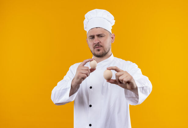 制服自信的年轻帅哥厨师身着厨师制服 手拿鸡蛋 看着隔离在橙色墙上的鸡蛋厨艺手握厨师