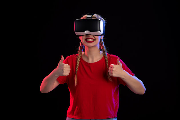 年轻女性在黑暗的墙壁上玩虚拟现实的年轻女性的正面视图游戏虚拟黑