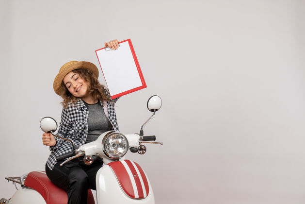 人坐在轻便摩托车上微笑的旅行女孩举着红色的剪贴板红色肖像剪贴板