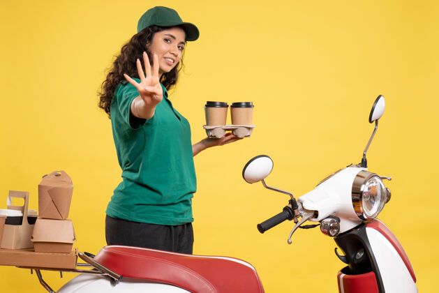 工作正面图身着绿色制服的女快递员 黄色背景上有咖啡 工作递送工作 食品女服务人员人音乐家食物