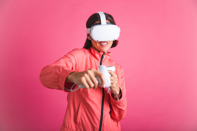 享受穿着运动夹克 戴着虚拟现实眼镜的年轻健美女士在粉红色的舞台上玩拳击比赛虚拟兴奋体验