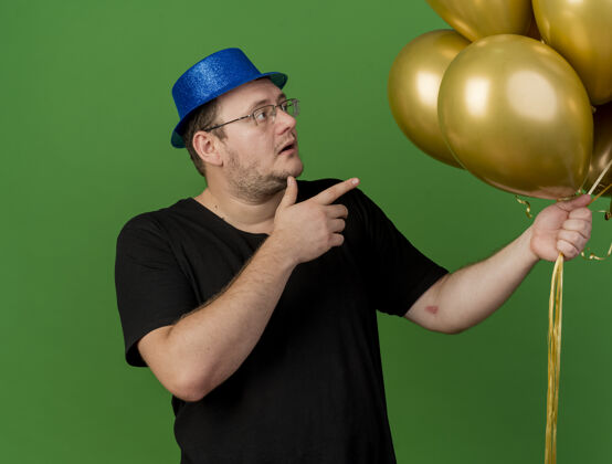 聚会戴着蓝色派对帽的戴眼镜的成年斯拉夫人惊讶地看着氦气球成人人斯拉夫