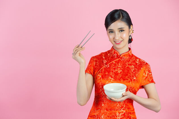 女孩美丽的亚洲女人快乐的微笑和吃在粉红色背景的中国新年碗复制空间微笑
