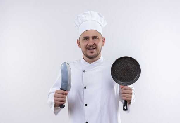 制服快乐的年轻帅哥厨师穿着厨师制服 拿着切肉刀和煎锅站在隔离的白色墙壁上 有复印空间烹饪手持欢乐