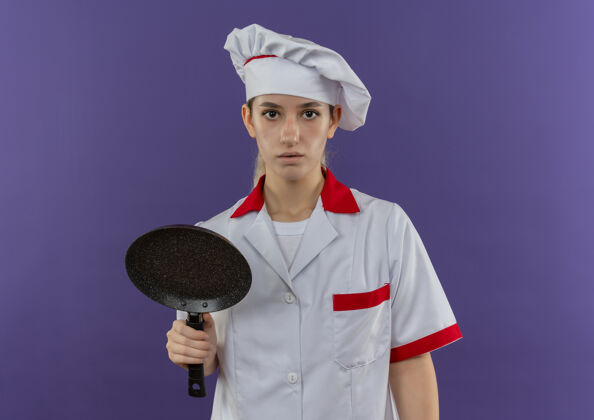 厨师令人印象深刻的年轻漂亮厨师在厨师制服举行煎锅看起来孤立的紫色墙上印象平底锅烹饪