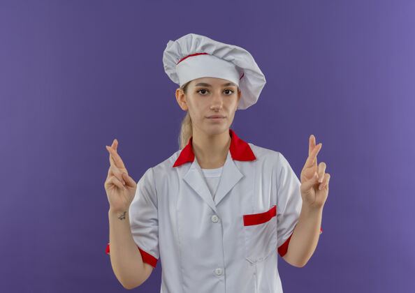 自信自信的年轻漂亮厨师穿着厨师制服做交叉手指手势看起来孤立在紫色的墙上手势漂亮烹饪