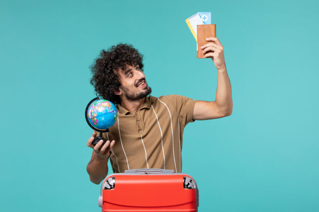 旅行前视图中的度假男子拿着地球仪和蓝色的机票人地球仪票