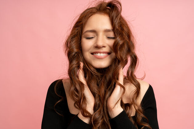 时尚美丽的红头发女人 闭着眼睛在粉红色的墙上摆姿势波浪形的头发完美的微笑快乐成人粉色