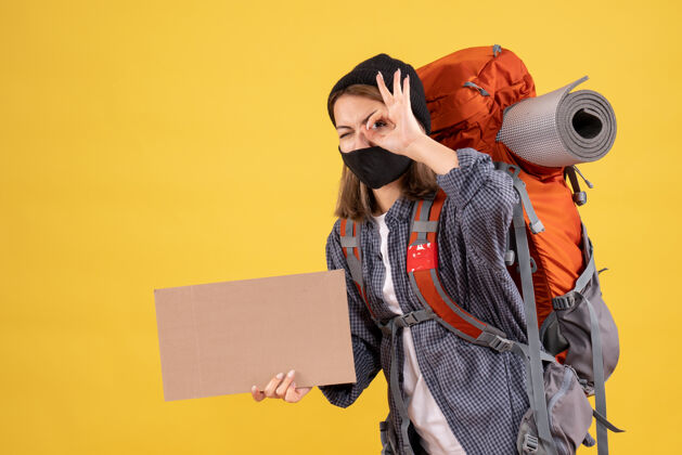 纸板一个带着黑色面具 背着硬纸板的背包的旅行女孩把ok标志放在眼前人背包成人