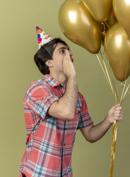绿色戴着生日帽的白种人帅哥高兴地站在一旁 手紧握着嘴看着氦气球气球嘴空间