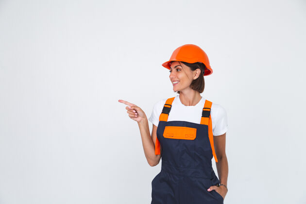 安全漂亮的女工程师在建筑防护头盔上自信地微笑着手指指向左边成功手臂头发