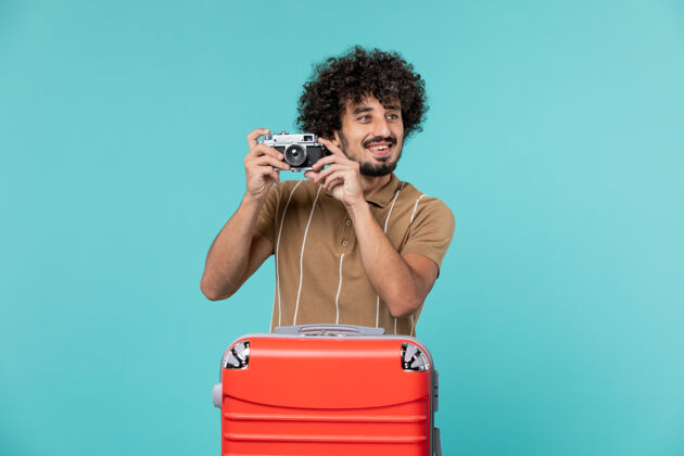 旅行带着红色手提箱的度假男人用蓝色的相机拍照红色行李蓝色