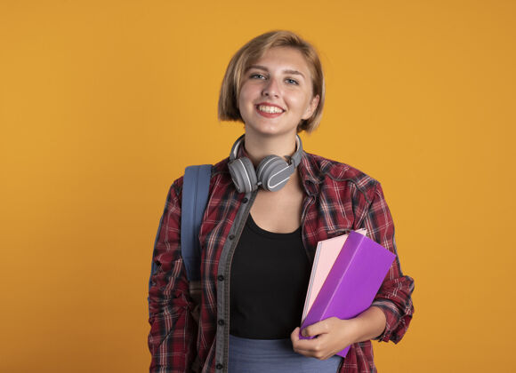 笔记本微笑着的年轻斯拉夫女学生戴着耳机背着书包拿着书和笔记本学生微笑空间