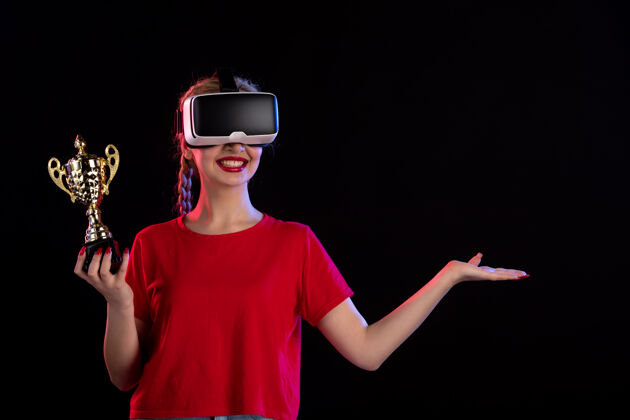 黑暗年轻女性在黑暗的墙上玩虚拟现实和赢得奖杯的正面视图年轻女性视图虚拟现实