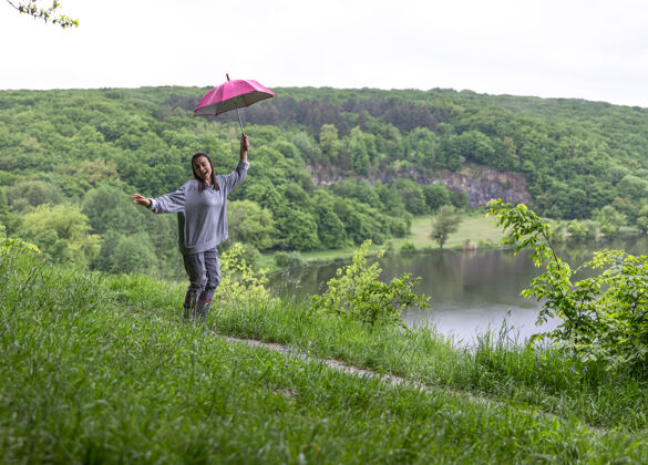 徒步旅行雨天 一个女孩打着伞在山区的湖边跳着湖泊雨伞绿色