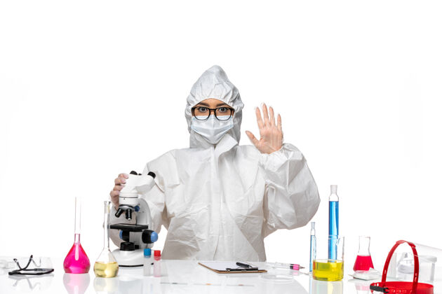 化学前视图年轻的女化学家穿着特殊的防护服 在白色背景上挥舞着显微镜病毒实验室的冠状病毒健康化学专业医生防护