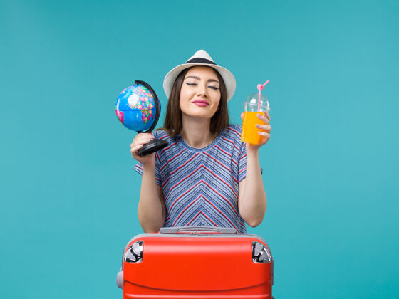 举行前景度假中的女人拿着果汁和地球仪在蓝色的背景海上航行暑假人微笑旅程