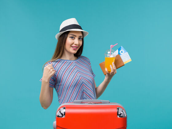 票前景：度假中的女人拿着她的红包 手里拿着机票和果汁 坐在蓝色的桌子上女包旅行