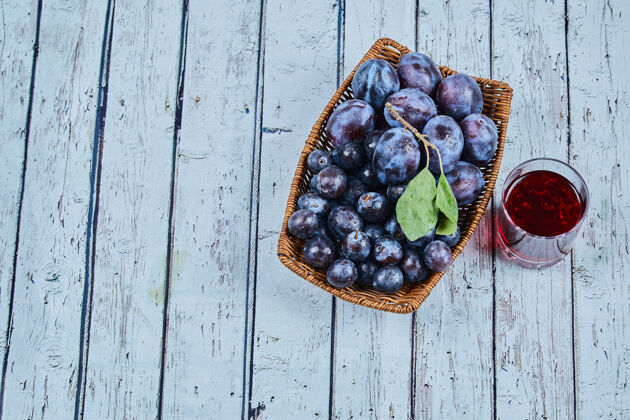 有机用一杯果汁把李子放在蓝色的篮子里花园健康紫色