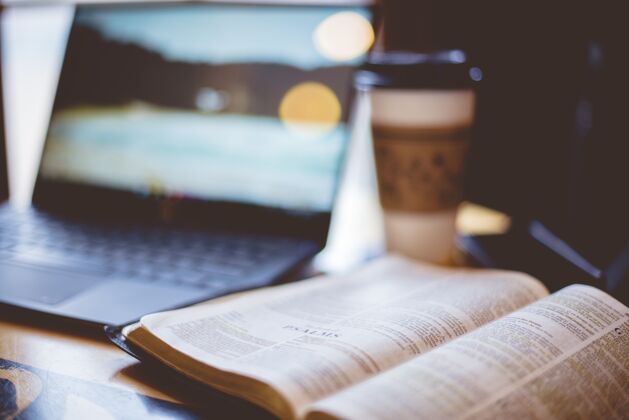 精神一本打开的圣经的特写镜头 一台模糊不清的笔记本电脑和一杯咖啡光建筑耶稣
