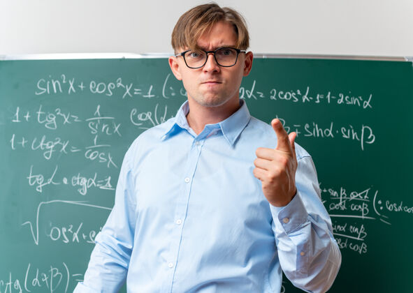 数学戴着眼镜的年轻男老师站在教室里的数学公式黑板旁 神情不快 怒气冲冲靠近老师男