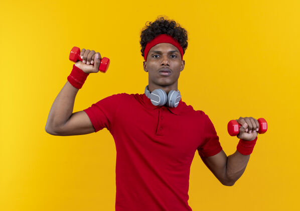 非裔美国人年轻的美国黑人运动型男子戴着头带和腕带 脖子上戴着耳机 用哑铃练习穿着年轻头带
