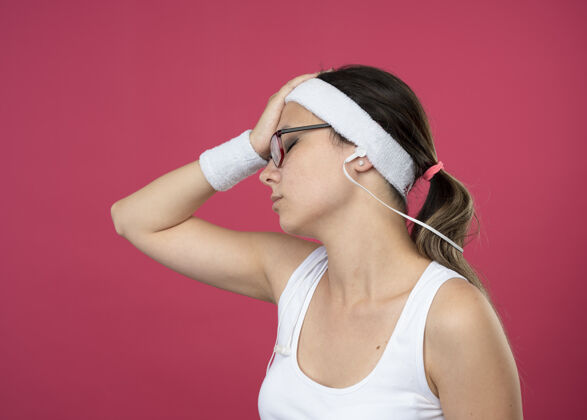 复制疲惫的年轻运动女孩戴着眼镜戴着耳机戴着头带和腕带把手放在额头上女孩运动头带