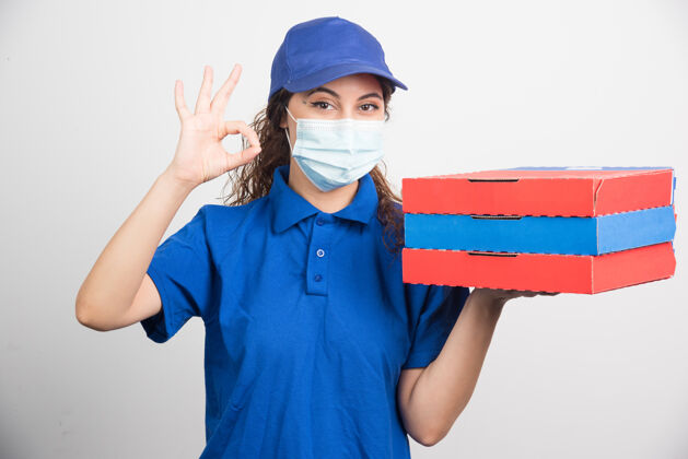 盒子送比萨饼的女孩拿着三个盒子 带着医用面罩 在白色上显示ok手势用餐面罩医疗