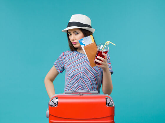 举行正面图：度假中的女人拿着果汁和蓝色背景的机票在海上避暑飞机上旅行旅程果汁女
