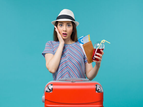 人前景度假中的女人拿着果汁拿着蓝色背景的机票 女人海上避暑 飞机旅行成人果汁票