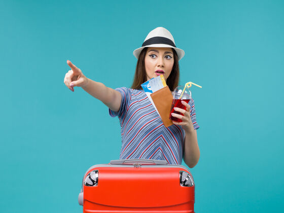 微笑前景度假中的女人拿着果汁和机票上蓝色背景的航程女海上避暑飞机肖像果汁票