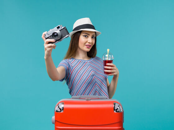 举行前景度假中的女人拿着果汁带着相机在蓝色的背景海上夏日航行飞机旅行肖像果汁微笑