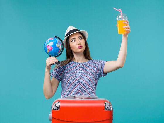 微笑前景度假女人拿着果汁和地球仪在蓝色书桌上海上旅行度假暑假旅行地球仪果汁成人
