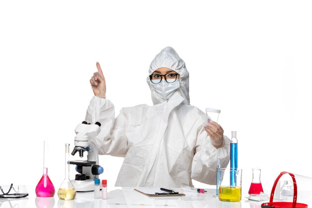 专业正面图：身穿特殊防护服的年轻女化学家拿着空瓶子在白色办公桌上 实验室里有化学病毒空实验室西装