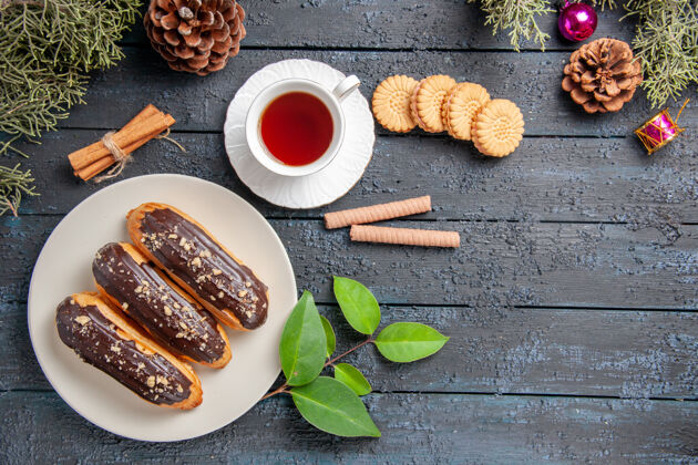 木头俯视图白色椭圆形圆锥体上的巧克力蛋糕圣诞玩具枞树树叶肉桂和不同的饼干在黑色木质地面上复制空间枞树树叶早餐