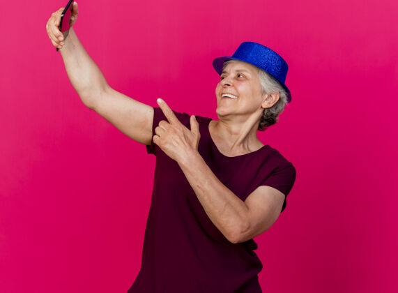 女人戴着派对帽的快乐的老太太看着粉色的手机老人聚会欢乐