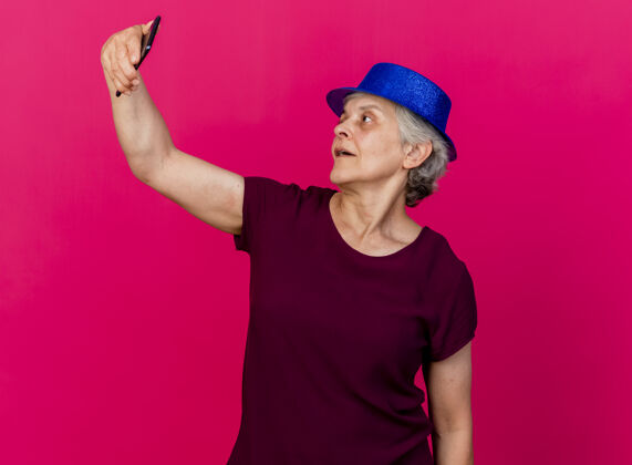 老人高兴的老妇人戴着聚会的帽子 拿着手机看着粉红色的帽子女人拜托