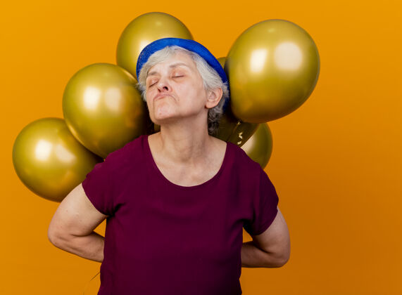 帽子得罪了戴着派对帽的老妇人 她闭着眼睛 把氦气球放在桔子上老人得罪了气球