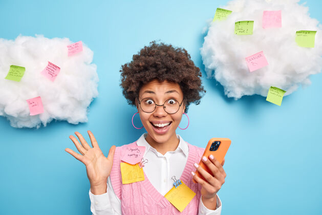 惊喜兴奋 快乐 勤奋的学生手持智能手机 发现优秀的考试成绩微笑着在蓝色的墙上 在云上贴上彩色的贴纸女性欣喜若狂技术