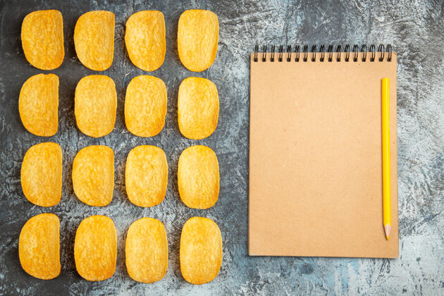 纸张俯视图：五个脆皮烤薯片排成一排 笔记本上有灰色背景的钢笔零食健康钢笔
