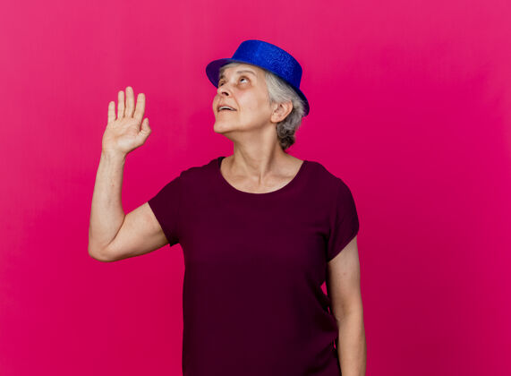 手戴着派对帽的老太太高兴地站起来 抬起手看着粉红色的脸帽子老人站起来