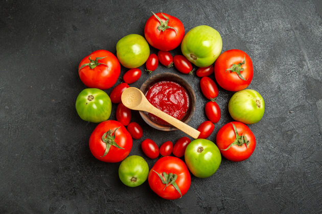 木头顶视图樱桃红色和绿色的西红柿围绕着一个碗和番茄酱和一个木勺在黑暗的地面上复制空间顶部食物周围