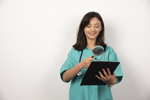 制服女医生用放大镜在白色背景上看剪贴板高质量的照片工人医生医疗