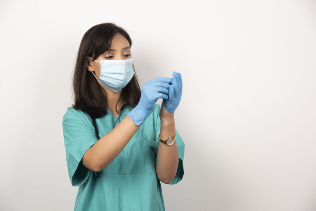 面罩戴着医用口罩的女医生看着白色背景上的手套高质量的照片医疗医生制服