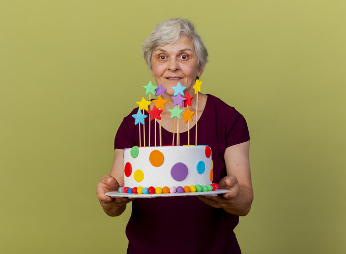姿势惊讶的老妇人把生日蛋糕孤立地放在橄榄绿的墙上橄榄生日市民