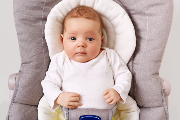 爱前视图好奇的新生婴儿穿着白色紧身衣躺在儿童保镖椅子休息椅子午睡
