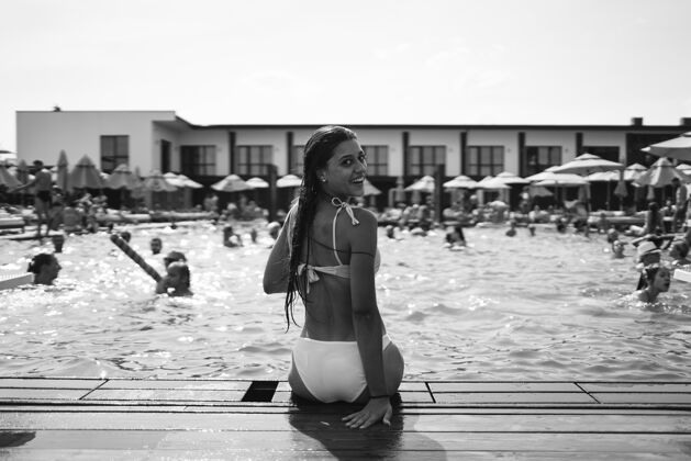 性感游泳池背景上穿着白色泳衣的年轻女子皮肤日光浴女性