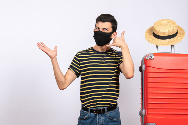 呼叫正面图：戴着黑色面具的年轻游客站在红色手提箱呼叫标志附近人黑色成人
